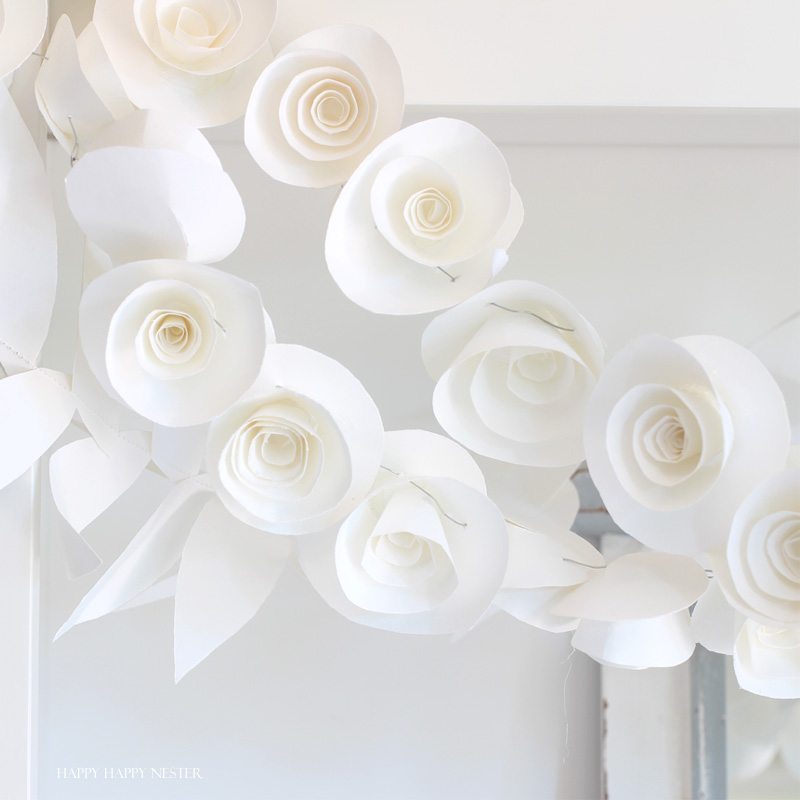 This fun paper garland DIY is not to be missed. You'll want to make both the leaf and rosettes garlands that you can hang anywhere in your home. Instant beauty wherever you place them. #craft #papercraft #paperflowers #garland #papergarland #weddingdecor #wedding