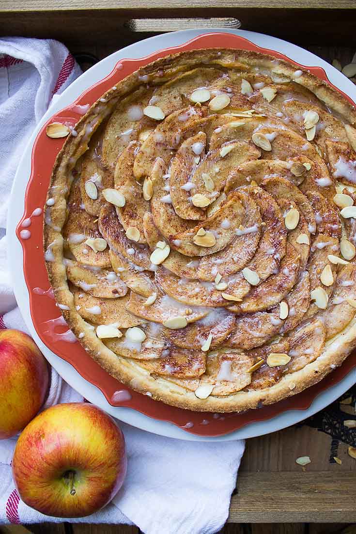 apple tart with almonds sprinkled on it. The tart is baked in a red pan