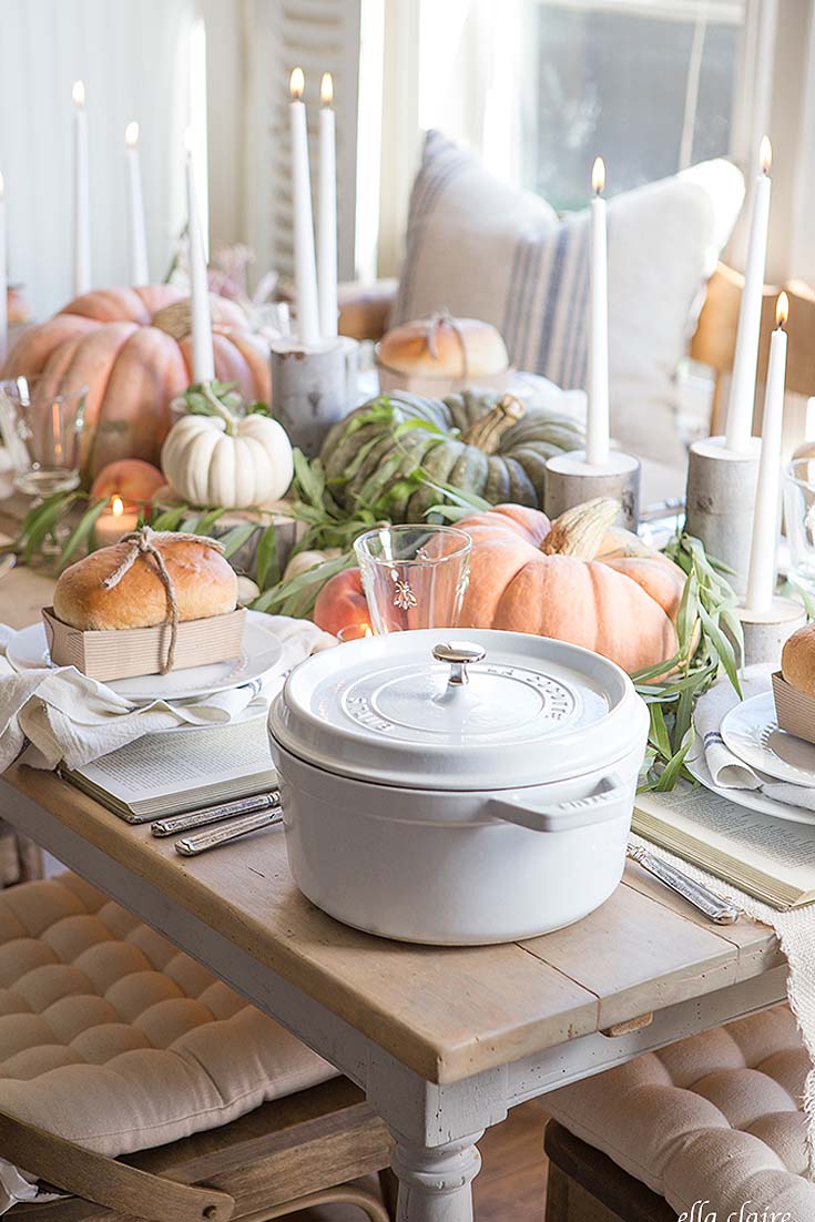 orange and green pumpkins on a table with white lit candlesticks