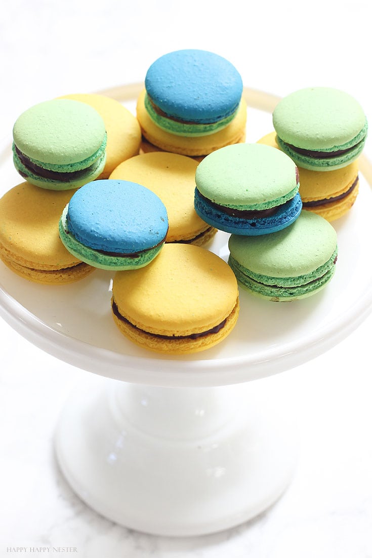 green, yellow and blue macarons on a white cake stand