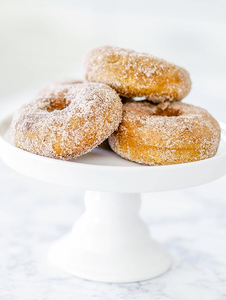 three cinnamon donuts on a white cake stand