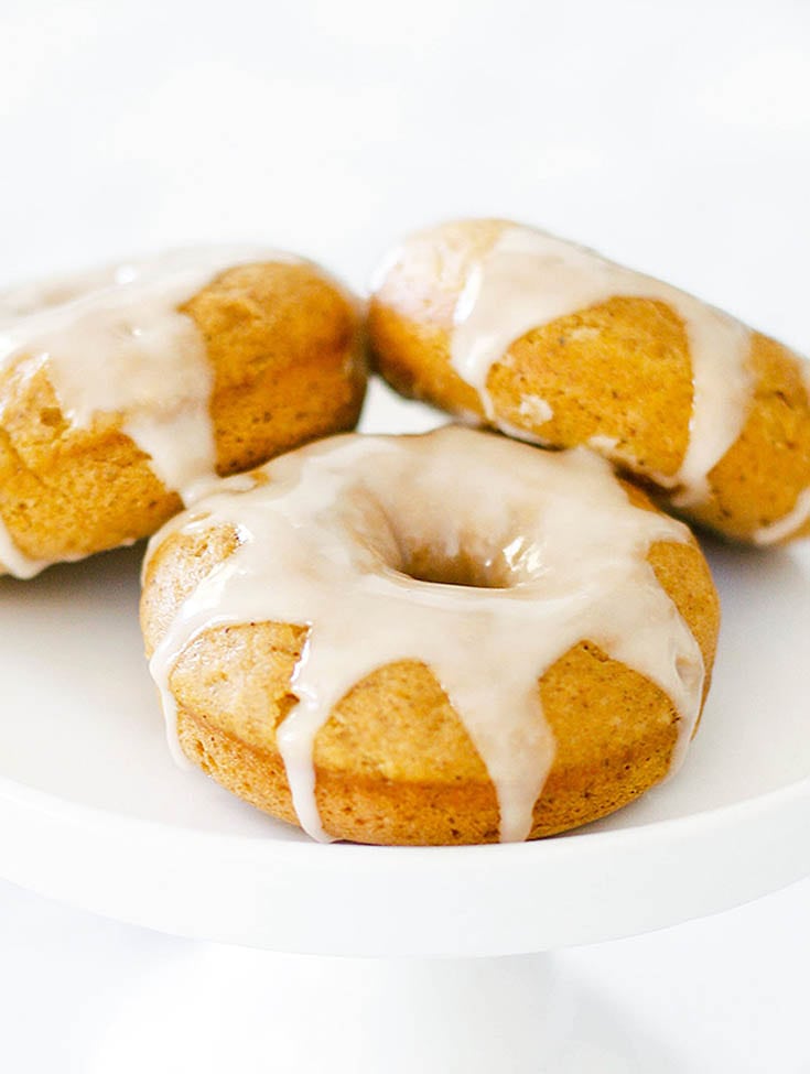 three pumpkin donuts with white icing on a white cake stand