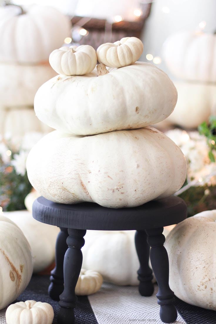 two white pumpkins stacked on top of each other on a black footstool