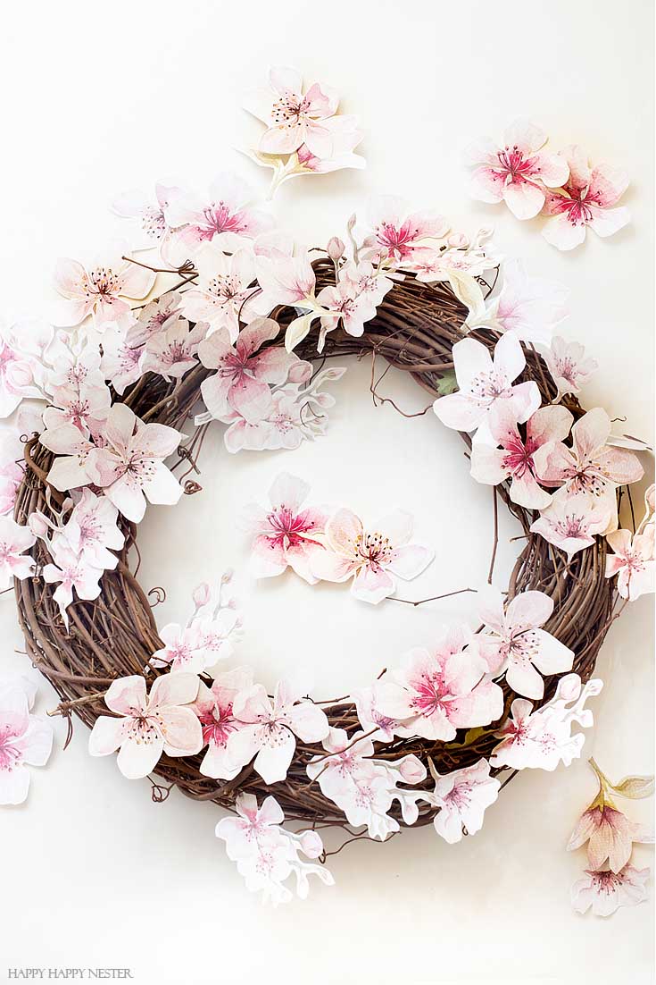 Make this easy and pretty wreath. This easy How to Make a Paper Flower Wreath DIY is perfect for the spring. This wreath uses watercolor cherry blossoms that you cut out and glue to a grapevine wreath. It is a simple wreath that is beautiful and nice year round. The supplies include a wreath, paper, scissors, glue, and ribbon. #crafts #wreaths #spring