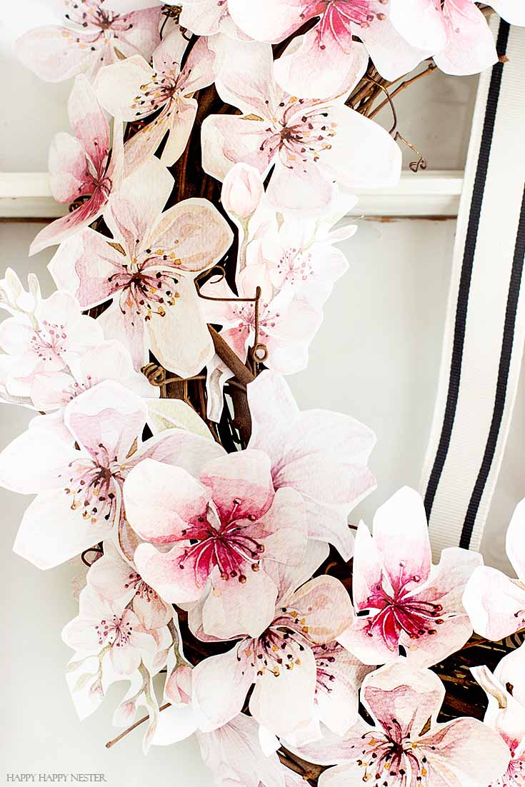 Watercolor flowers cover this spring wreath. This easy How to Make a Paper Flower Wreath DIY is perfect for the spring. This wreath uses watercolor cherry blossoms that you cut out and glue to a grapevine wreath. It is a simple wreath that is beautiful and nice year round. The supplies include a wreath, paper, scissors, glue, and ribbon. #crafts #wreaths #spring
