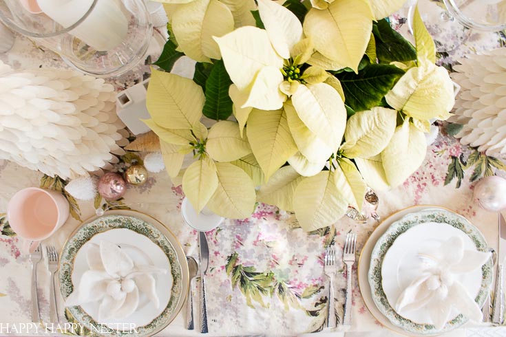 Use white Christmas poinsettias on your holiday tables. Also, when it comes to tablecloths, use vintage material for a romantic shabby chic cottage style. Find out these table ideas for Christmas decorating. This table decor is feminine and vintage all rolled up in one. #shabbychic #Christmasvintage #vintageornaments #whitepointsettias