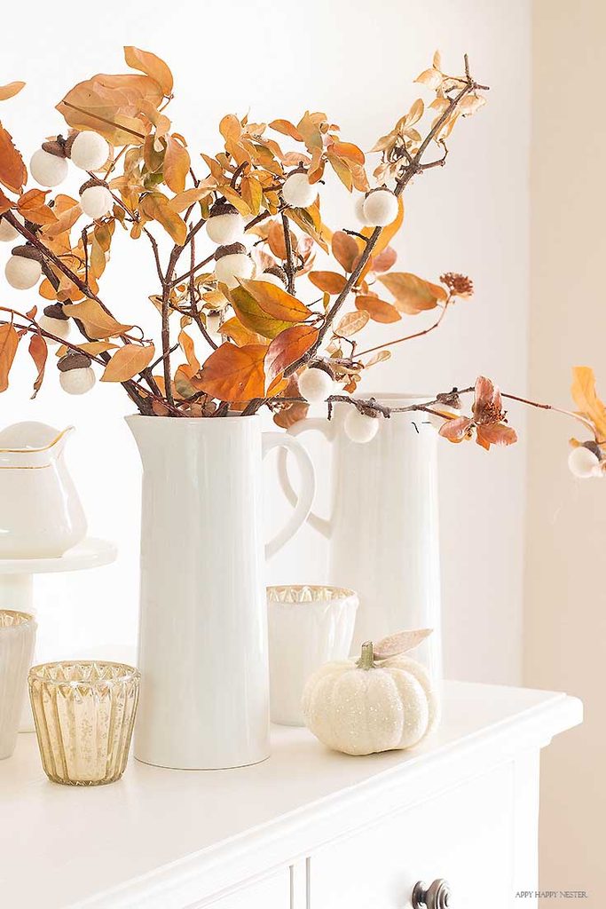 Branches decorated with felt acorns displayed in white pitchers on a fall mantel