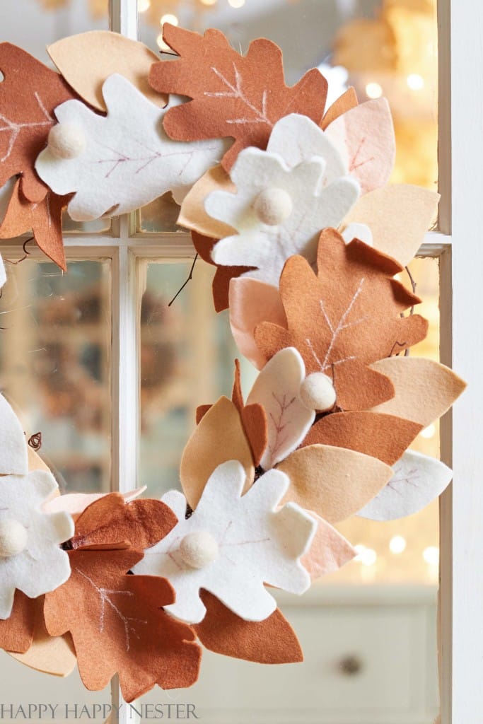 A wreath of felt leaves in shades of cream, tan, and brown hanging on a glass door as a fall leaf craft idea.