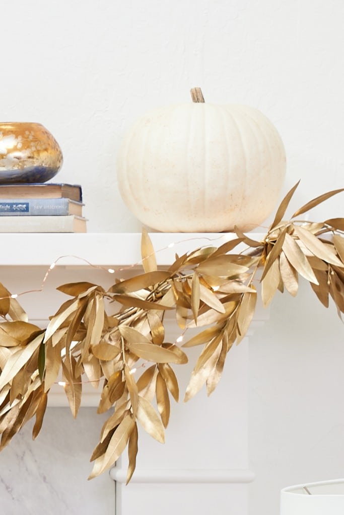 Metallic gold bay leaf garland decorating a fall mantel with white pumpkins