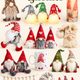 A collection of Christmas gnome decor, including plush figurines, a lit candle, a coffee mug, and a hanging garland.