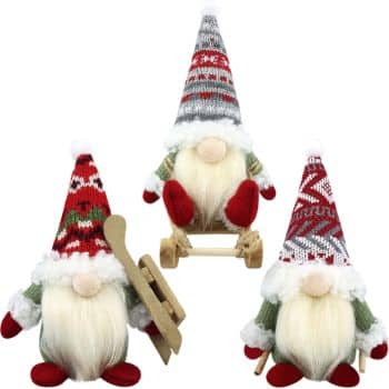 Three Christmas gnomes wearing patterned knit hats, one sitting on a wooden sled, one holding a pair of wooden skis, and one standing with poles.