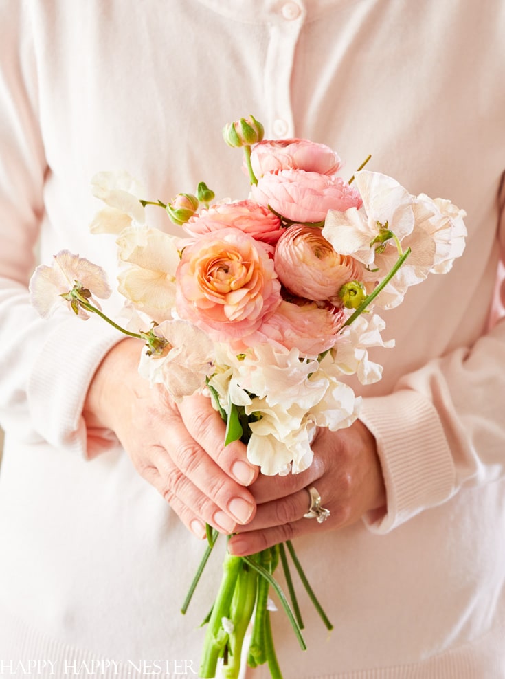small bouquet of flowers held in front of a woman dressed in a pink sweater