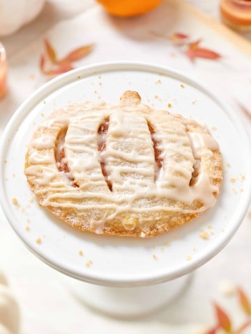 Mini pumpkin hand pie with icing drizzle on a white cake stand