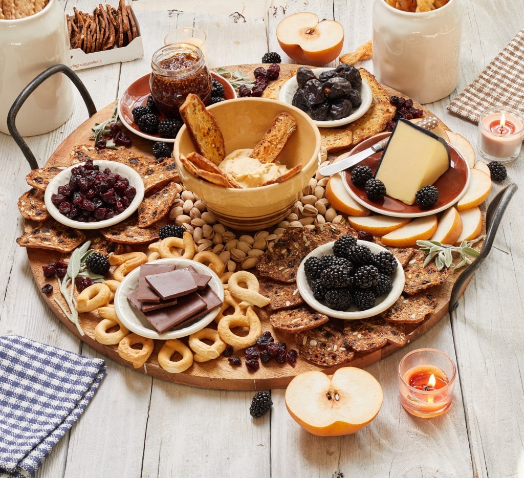 a collection of crackers, fruit and cheeses on a charcuterie board