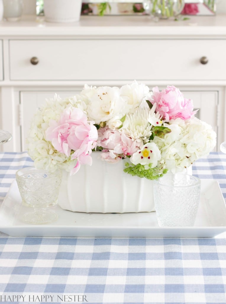 pink and white peony centerpiece on a dining room table with a blue and white gingham tablecloth