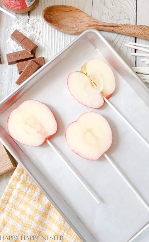 three cut apples slices with lollipop sticks on a baking tray