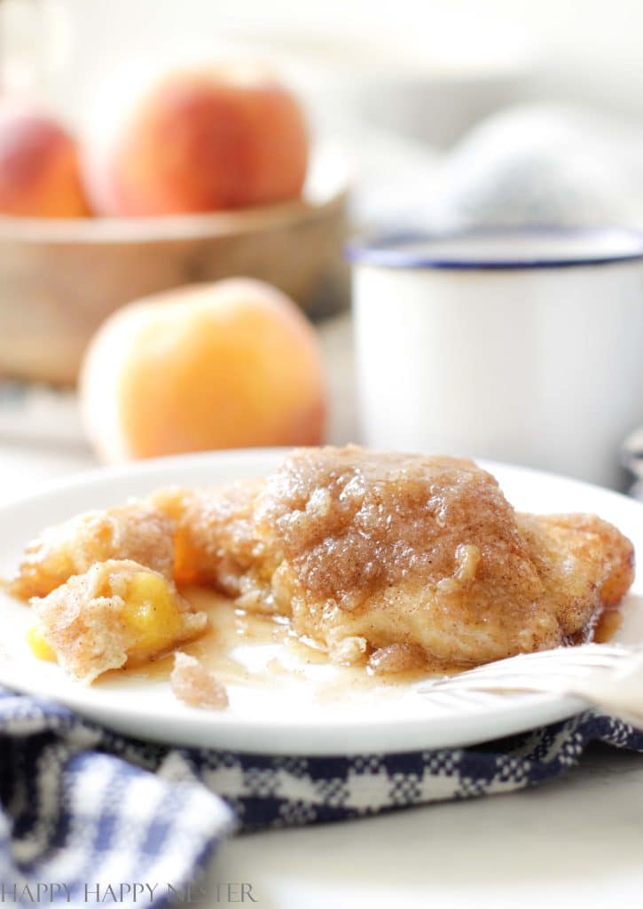 A close up of a peach dumpling that is cut in half. The peach and flakey dough are bathed in a rich caramel sauce. All of it is on a white plate with a fork to the side. 