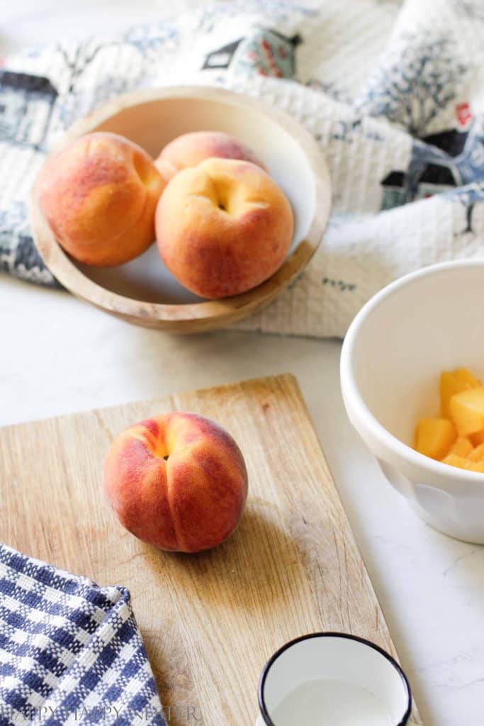 A peach is sitting on a small wooden cutting board ready to make the peach dumplings with crescent rolls recipe. 