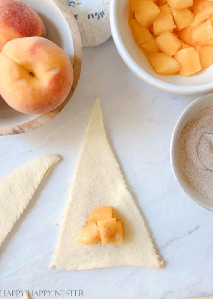 A triangle slice of Pillsbury crescent roll dough with a small pile of cubed peaches on the wider end of the dough.