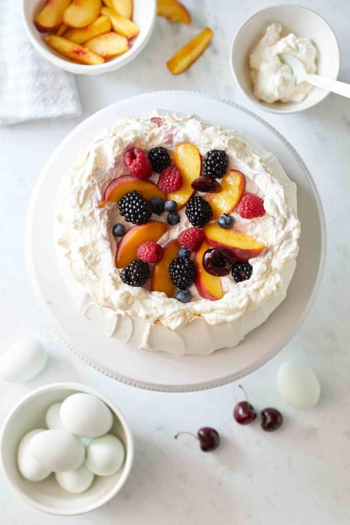 view of the top of the pavlova with the fresh fruit. All of it on a white cakestand.