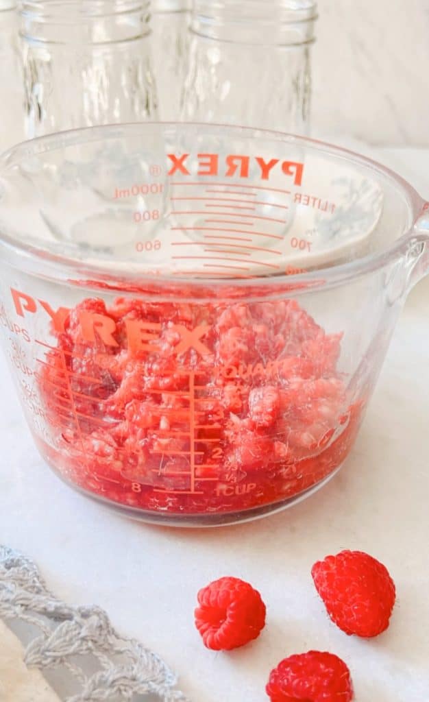 the recipe for raspberry freezer jam shows a photo of the raspberries all mashed in a pyrex glass container