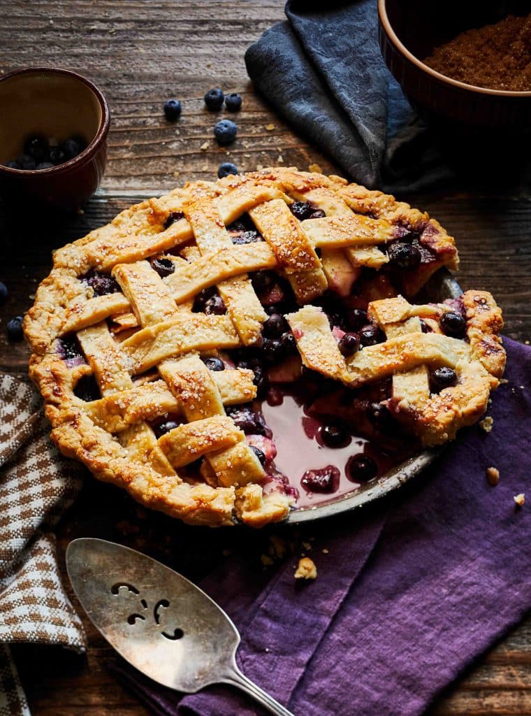 A cut into pie with lattice crust on a table with an antique spatula