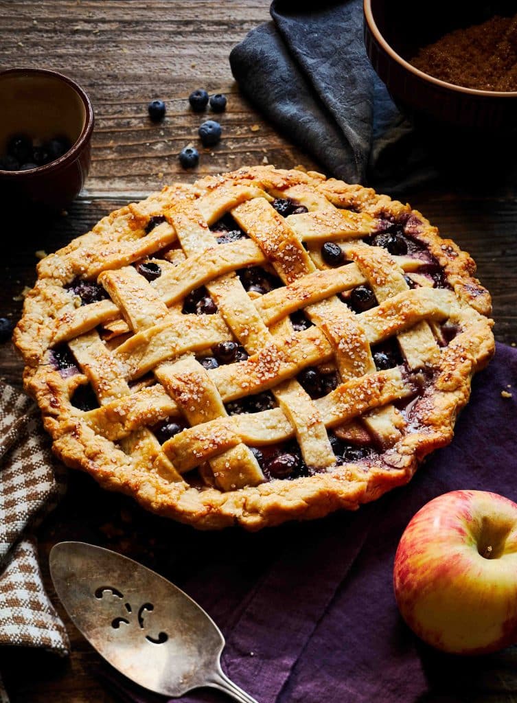 A photo of a lattice topped apple blueberry pie on a dark wooden table.