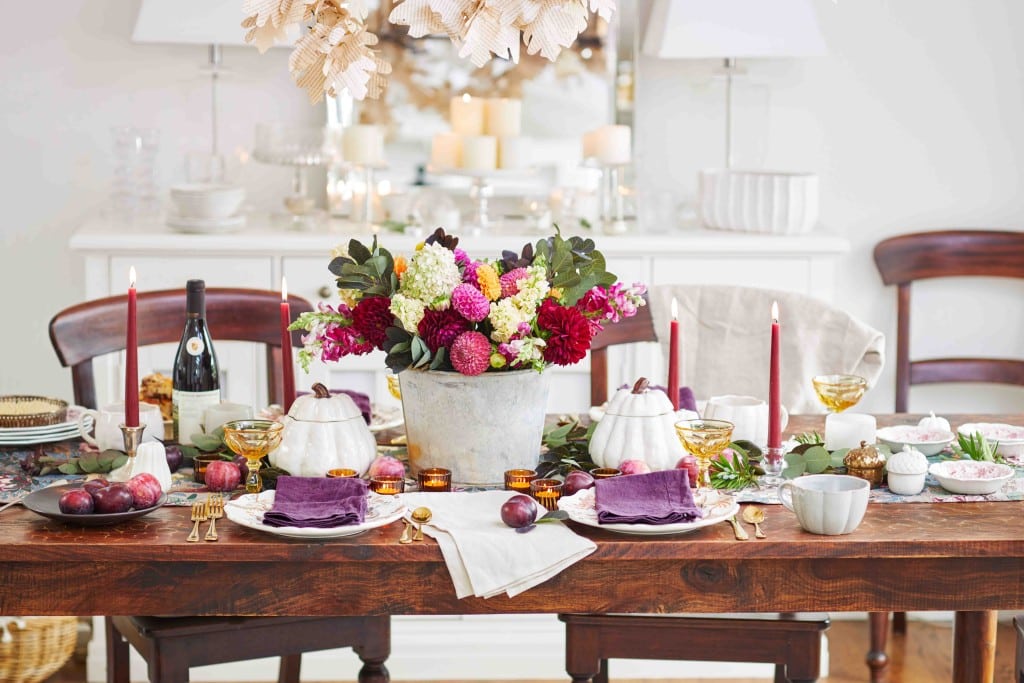 a horizontal shot of a fall dining room table decorated with maroon candles, purple napkins and amber tea lights.