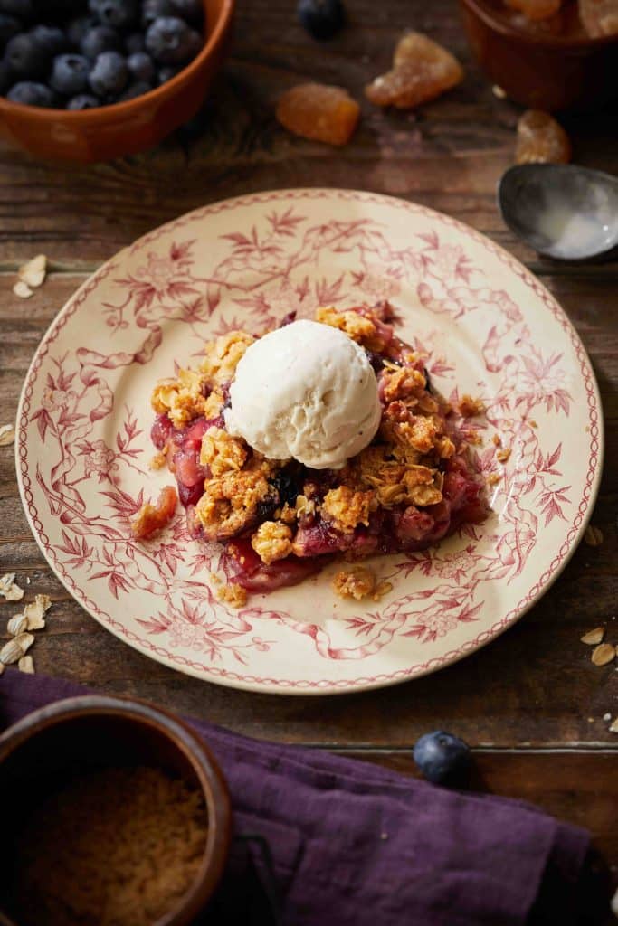 a slice of apple blueberry crisp on a red vintage plate. All of it on top of a wooden table