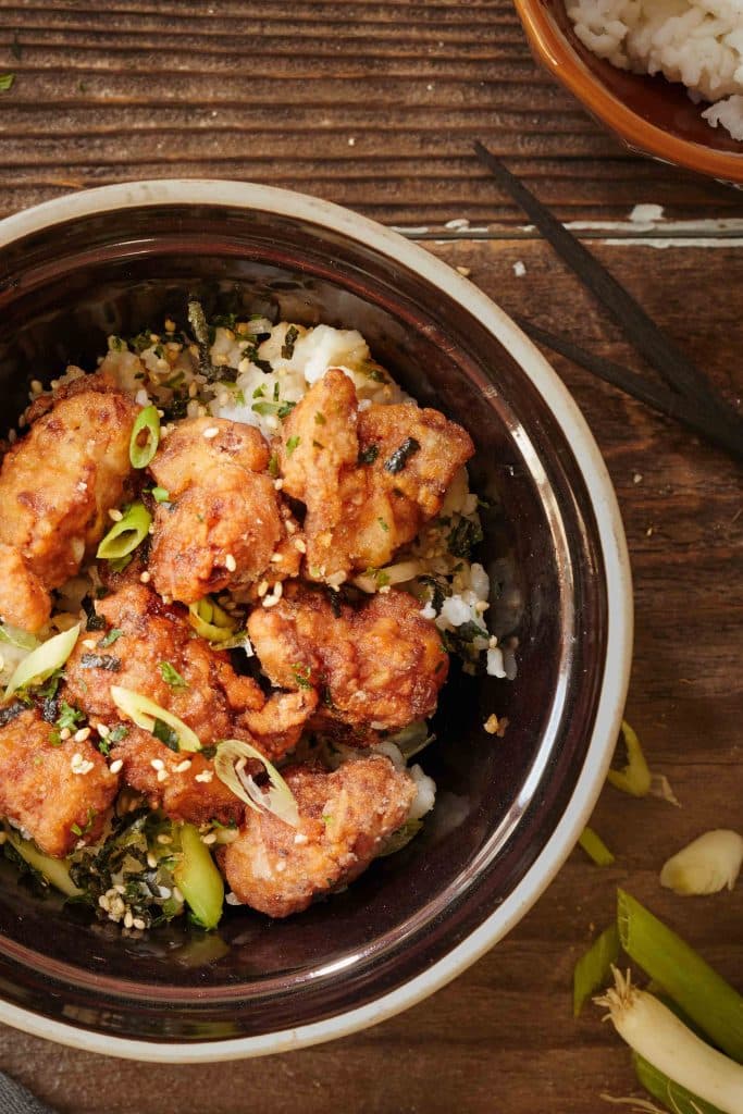 Tori Karaage Don in a black bowl with chopsticks to the right of it. 