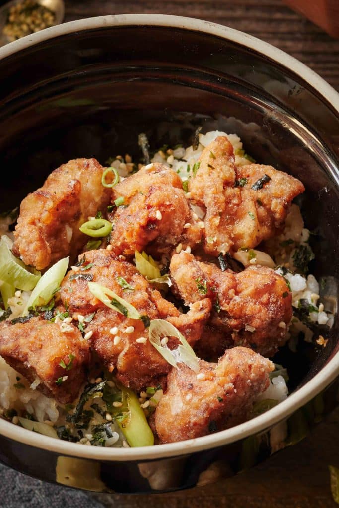 fried japanese chicken in a black bowl with rice on the bottom