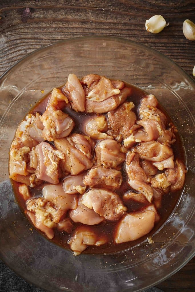 boneless skinless chicken bite-size pieces soaking in a marinade in a glass bowl.