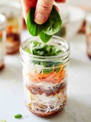 mason jar instant noodles and a hand adding spinach