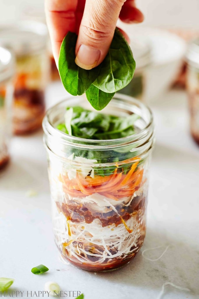 mason jar instant noodles and a hand adding spinach