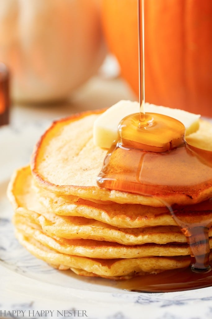a close up of buttermilk pumpkin pancakes with syrup being poured on top