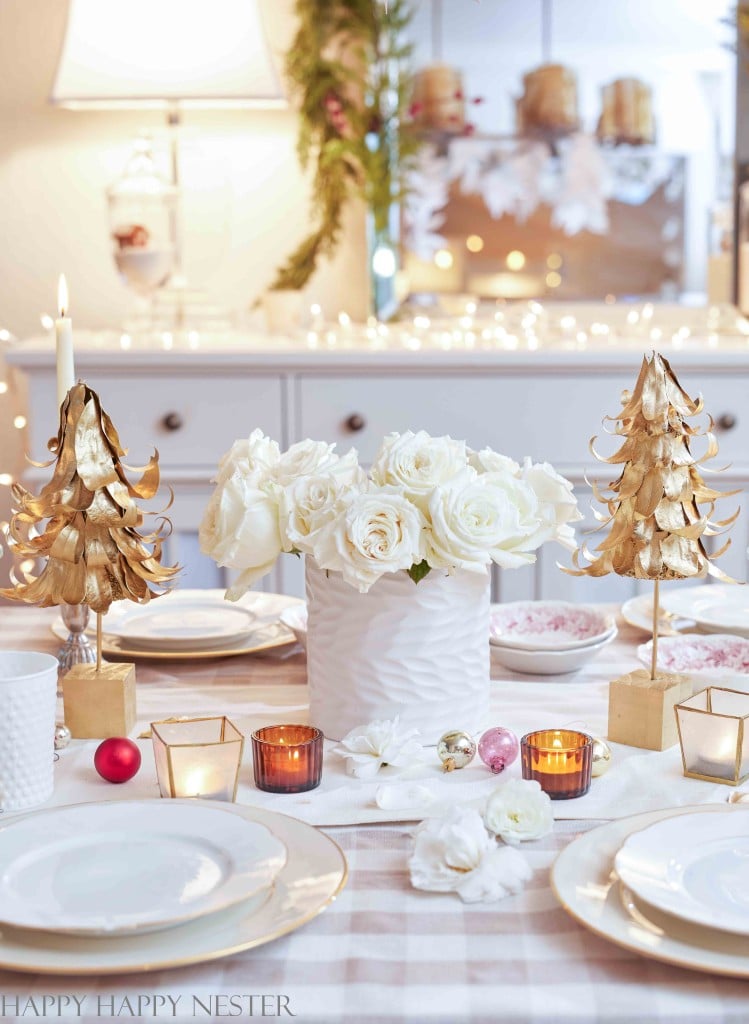 a pretty table with white roses in a white vase and the two gold tabletop christmas trees on each side of the vase