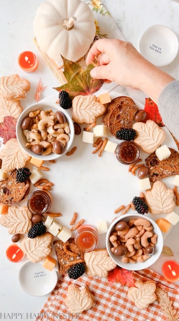 placing leaves on a charcuterie board shaped like a wreath