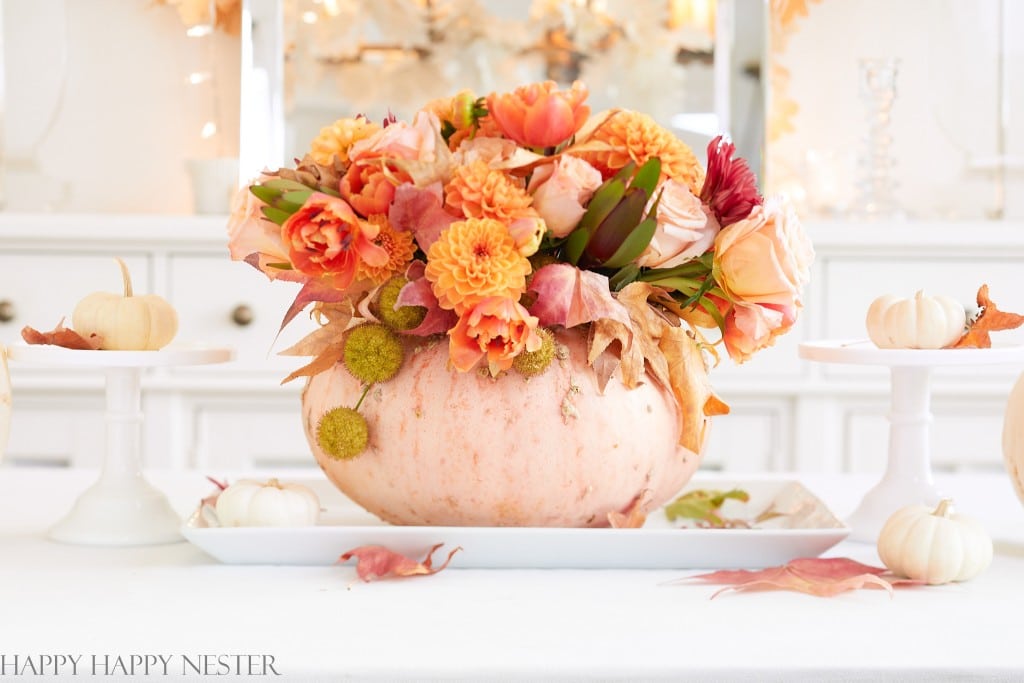 a pumpkin holding a fall flower arrangement as a centerpiece on a white table