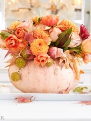 a pumpkin vase holding a fall flower arrangement as a centerpiece on a white table