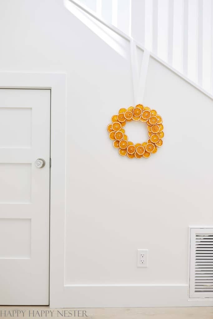 A Christmas wreath with orange slices on a white wall in a hallway with stairs