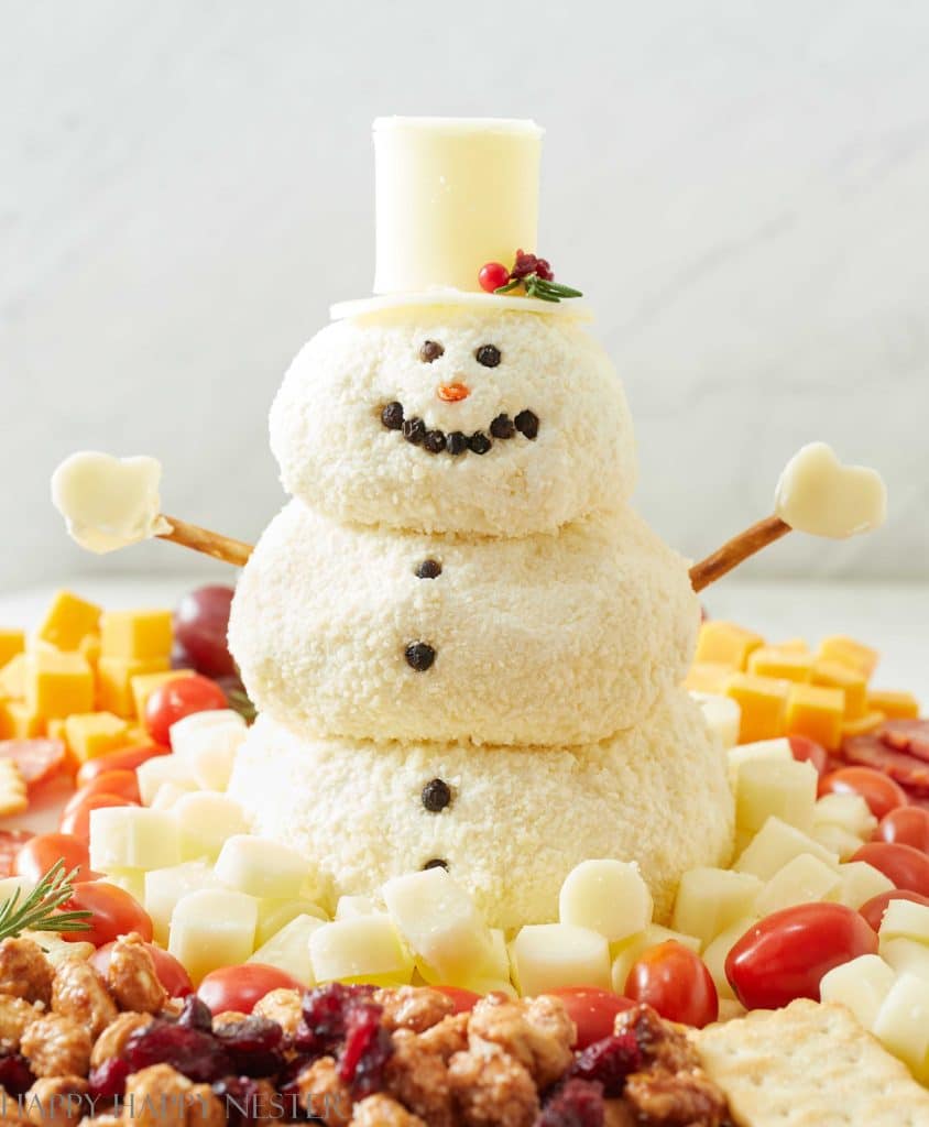 easy snowman cheeseball recipe with a snowman sitting in the middle of a fruit and cheese charcuterie board