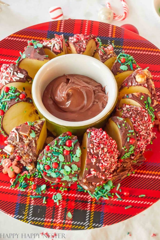 a cakestand full of chocolate covered apples for Christmas with fudge sauce in the middle