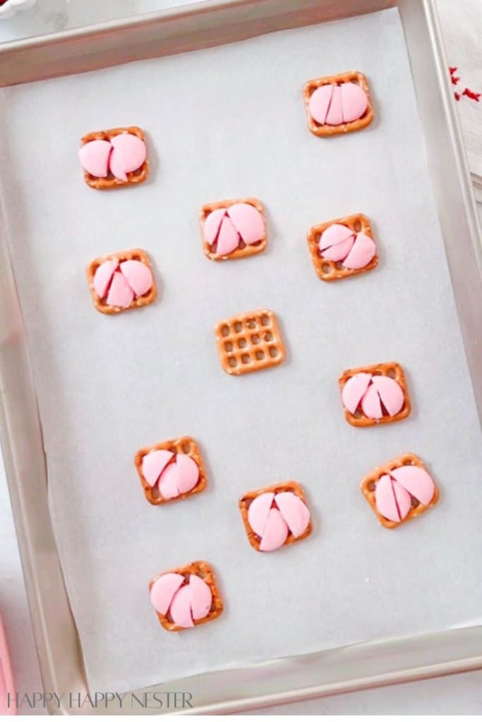 pretzels on a baking sheet with chopped up pink chocolate on the tops of them. they are waiting to be baked