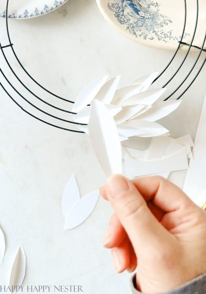 a person holding up a paper leaf that is folded in the middle. this leaf will go on the wire wreath form to make this january winter wreath