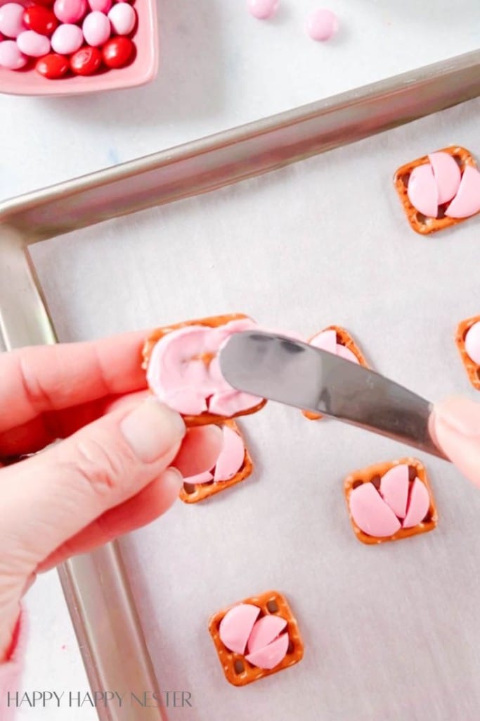 spreading pink melted chocolate on a square pretzel