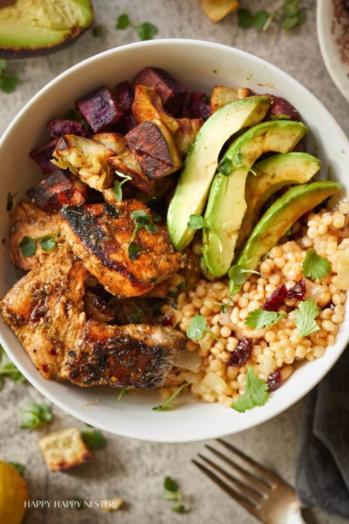 close up photo of salmon, avocados, couscous and roasted yams. all in a white bowl