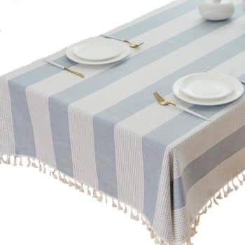 A rectangular table covered with a striped tablecloth in light blue and white, featuring fringe along the edges. Perfect for simple porch decor, the table is set with white plates, gold utensils, and a white decorative vase—find similar looks on Amazon.