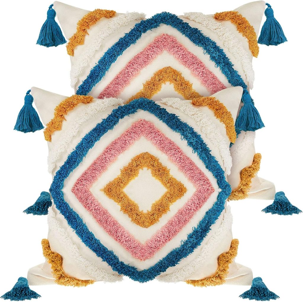 Two decorative square pillows with white fabric, featuring diamond patterns in blue, pink, and yellow tufted textures. Each corner has a blue tassel. These amazon boho throw pillows are stacked with fronts visible.