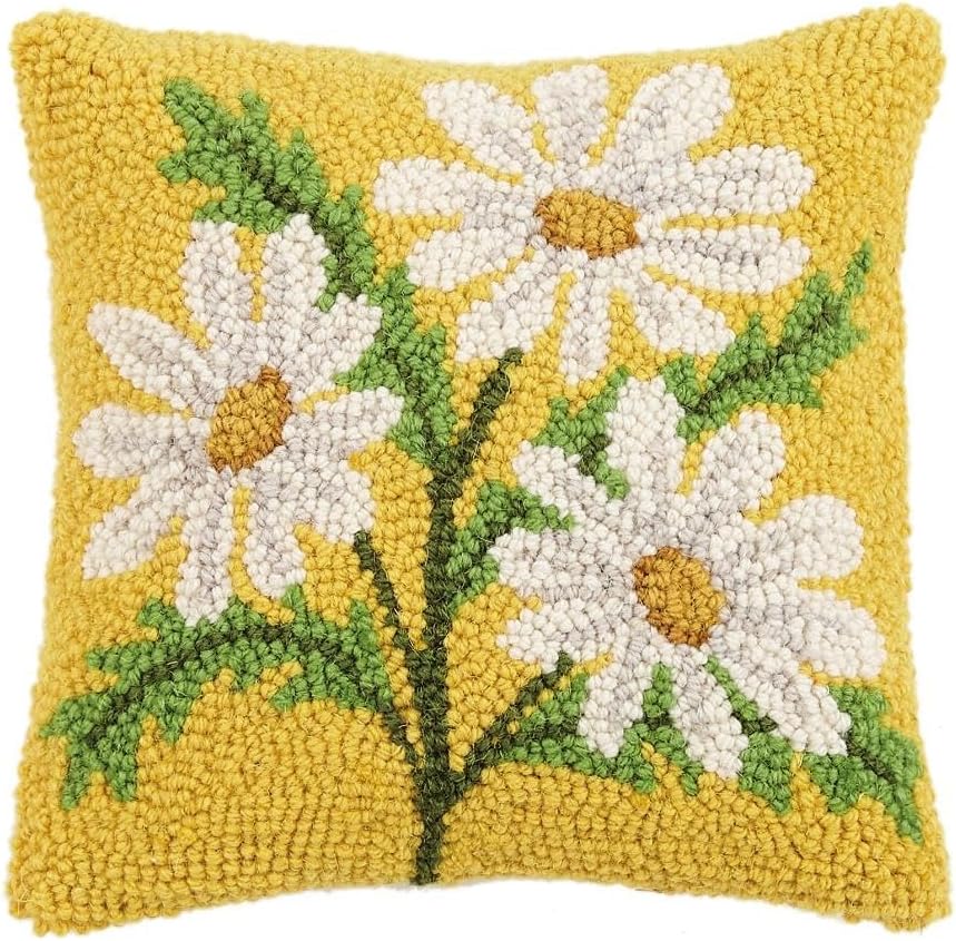 A square yellow springtime throw pillow featuring a textured design of three white daisies with yellow centers and green stems and leaves in a hooked, handmade style.