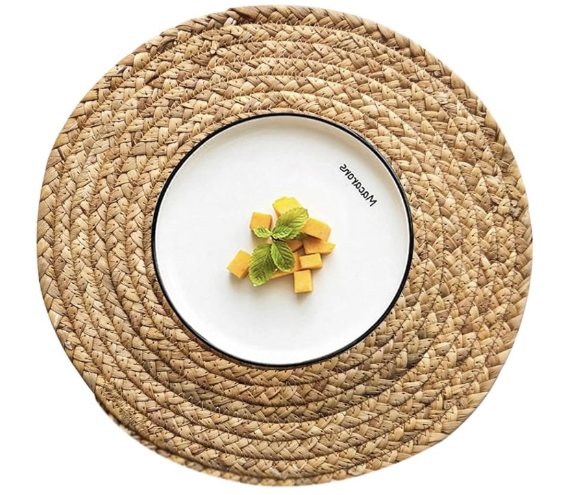 A white plate with a few small cubes of mango and a sprig of mint rests on a round, woven straw placemat, offering inspiration for subtle rattan decor ideas.